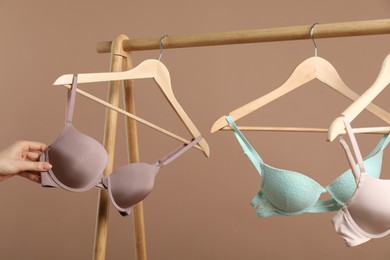 Photo of Woman choosing beautiful bra near rack on dark beige background, closeup