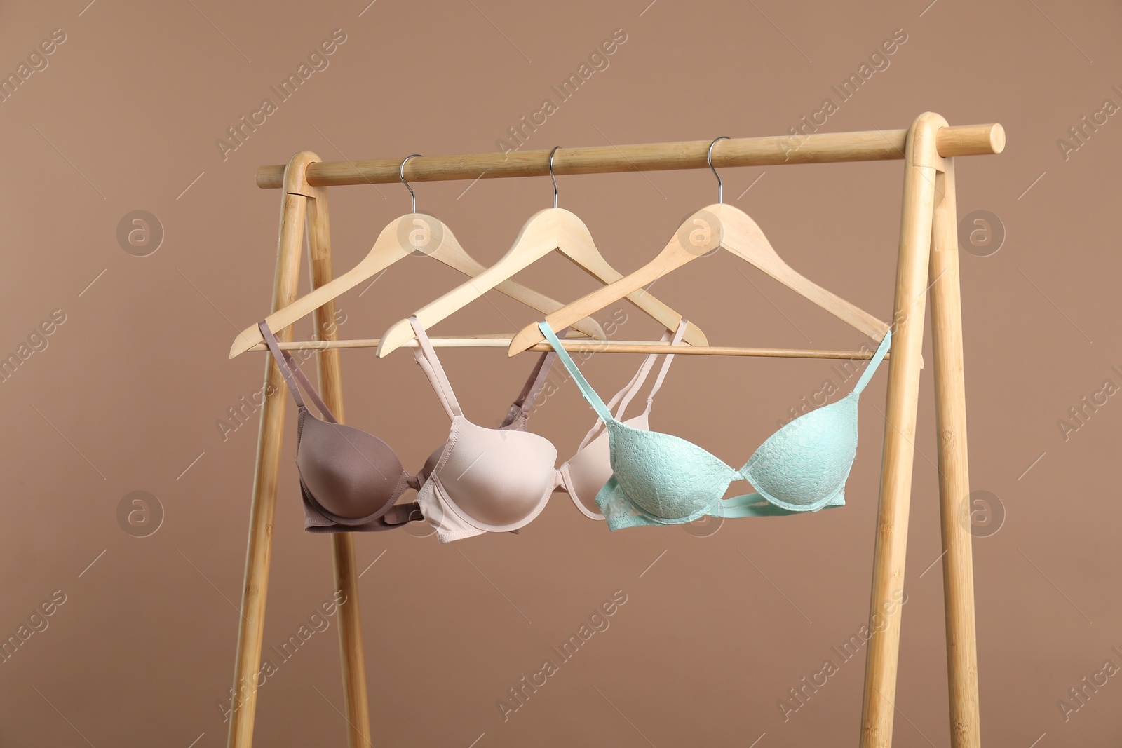 Photo of Hangers with beautiful bras on wooden rack against dark beige background