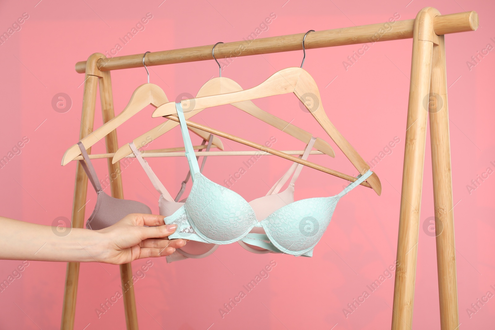 Photo of Woman choosing beautiful bra near rack on pink background, closeup