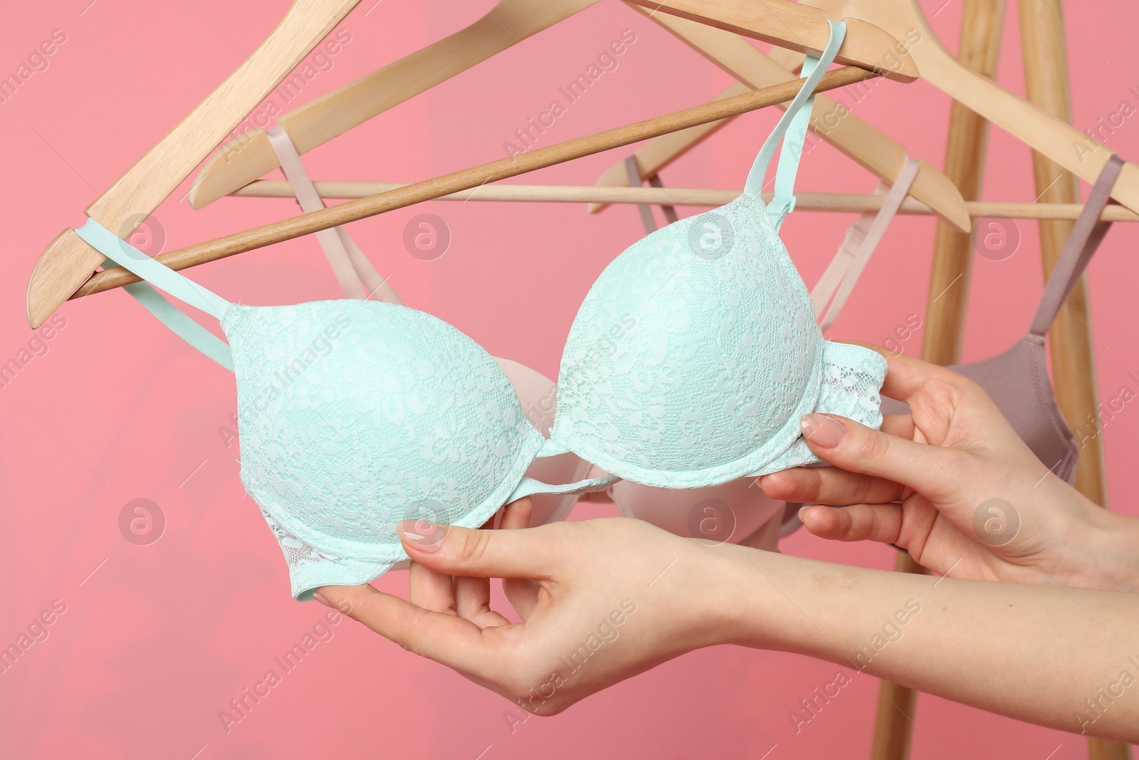 Photo of Woman choosing beautiful bra near rack on pink background, closeup