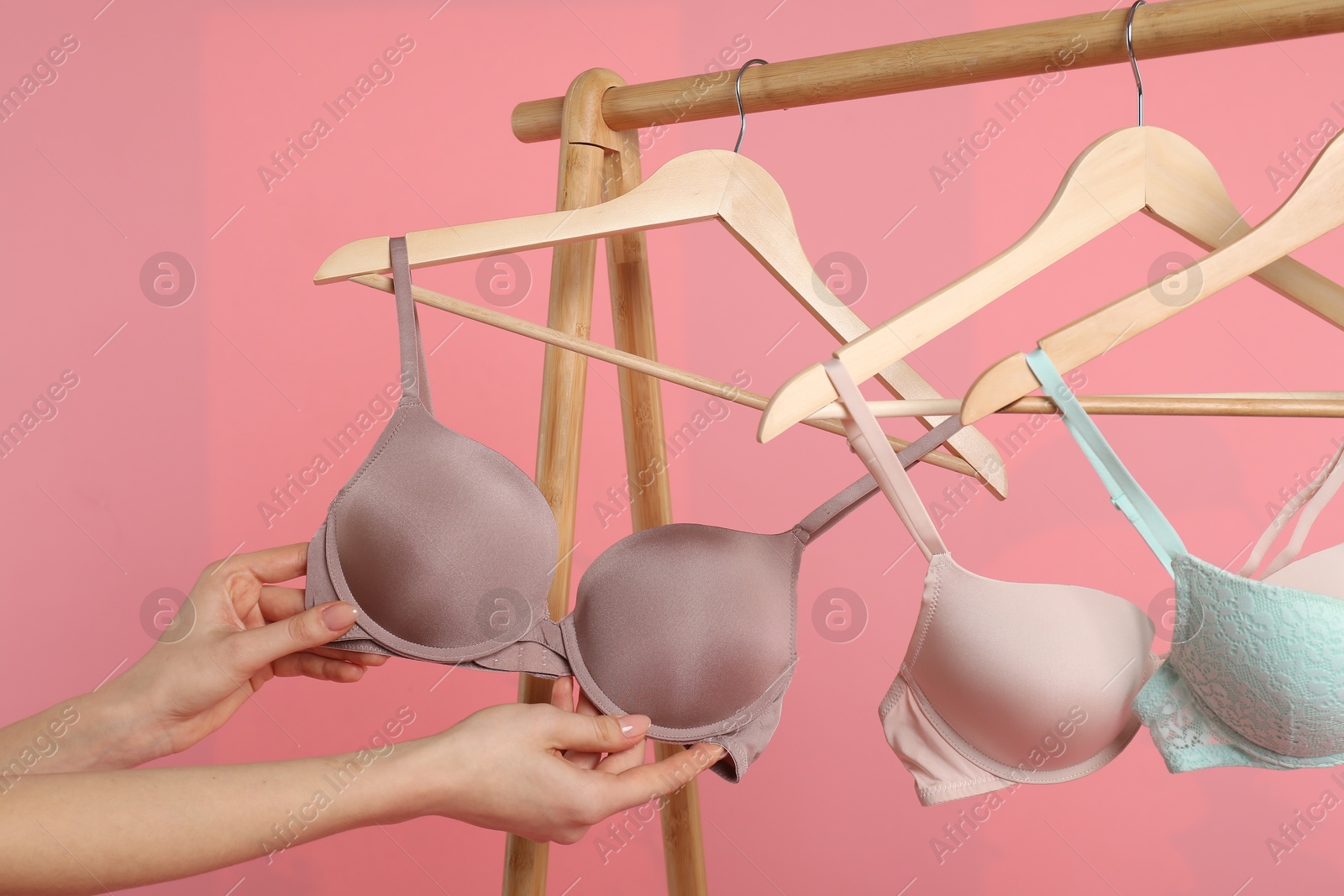 Photo of Woman choosing beautiful bra near rack on pink background, closeup