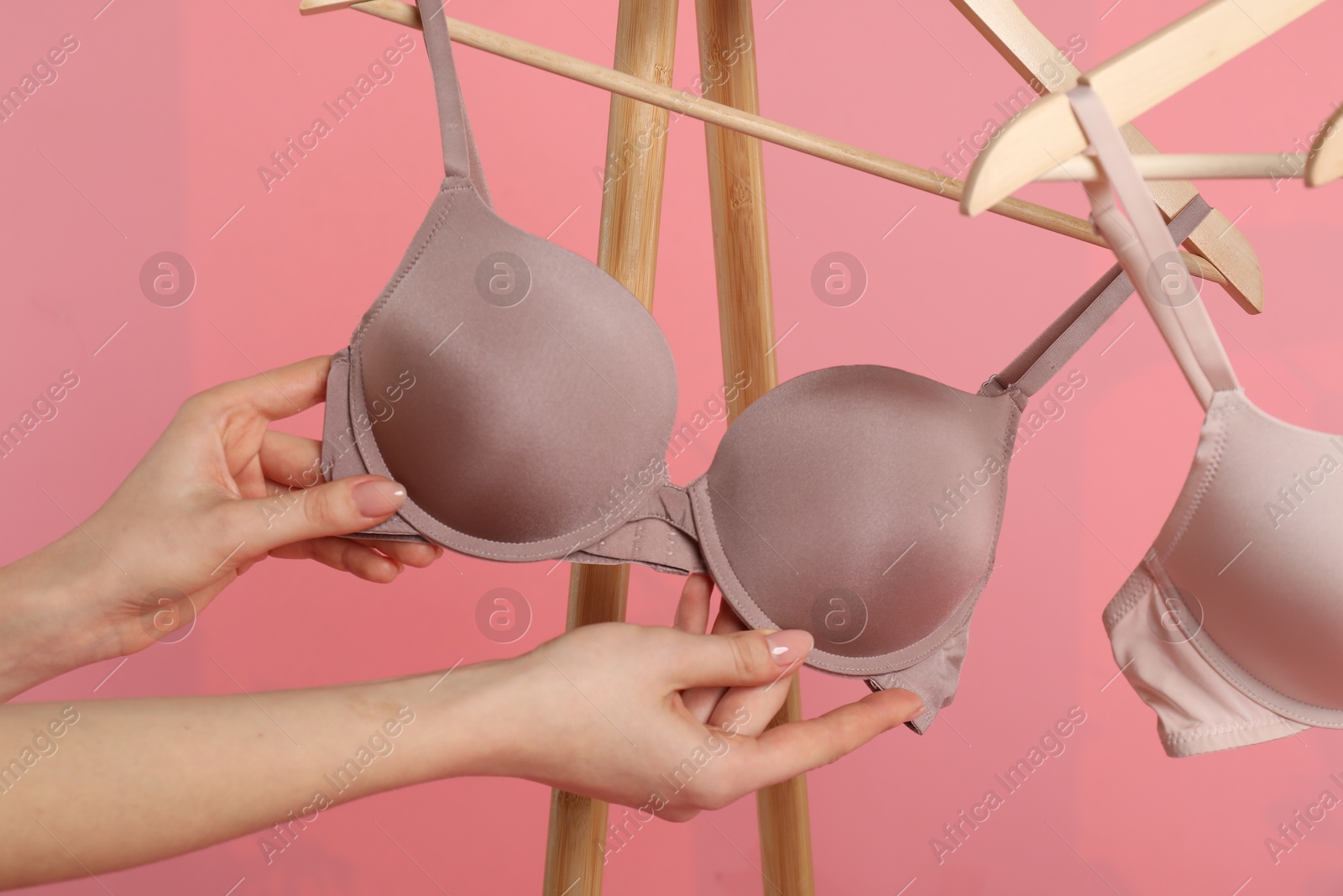 Photo of Woman choosing beautiful bra near rack on pink background, closeup