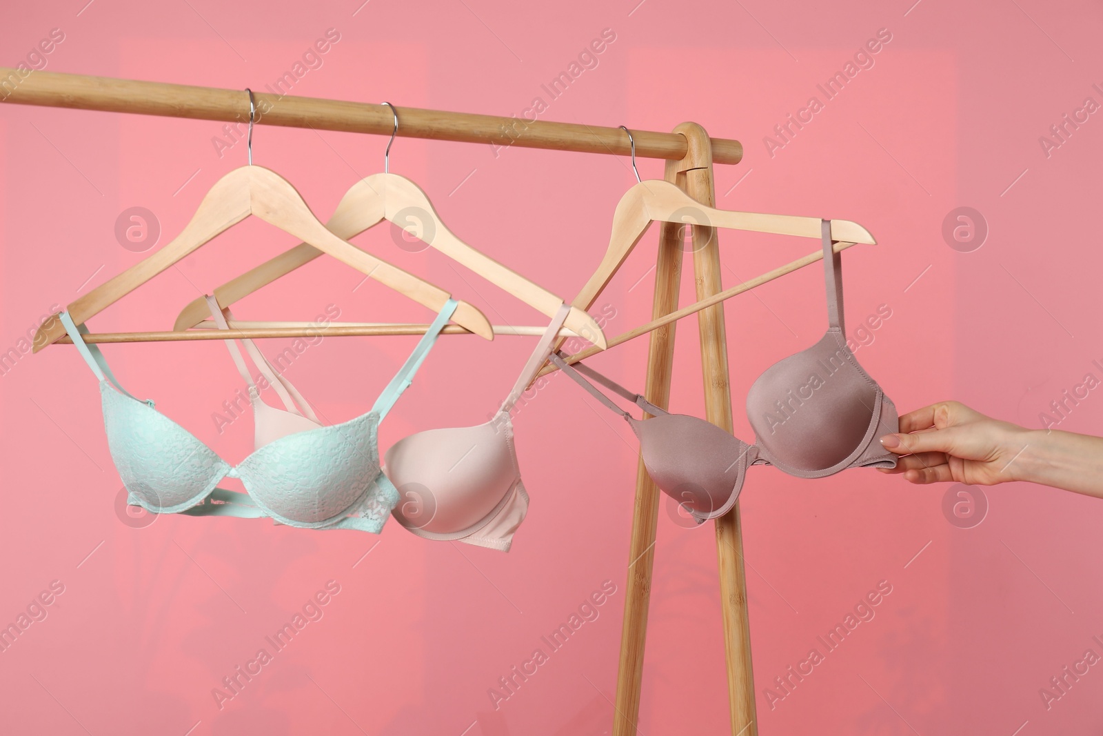 Photo of Woman choosing beautiful bra near rack on pink background, closeup