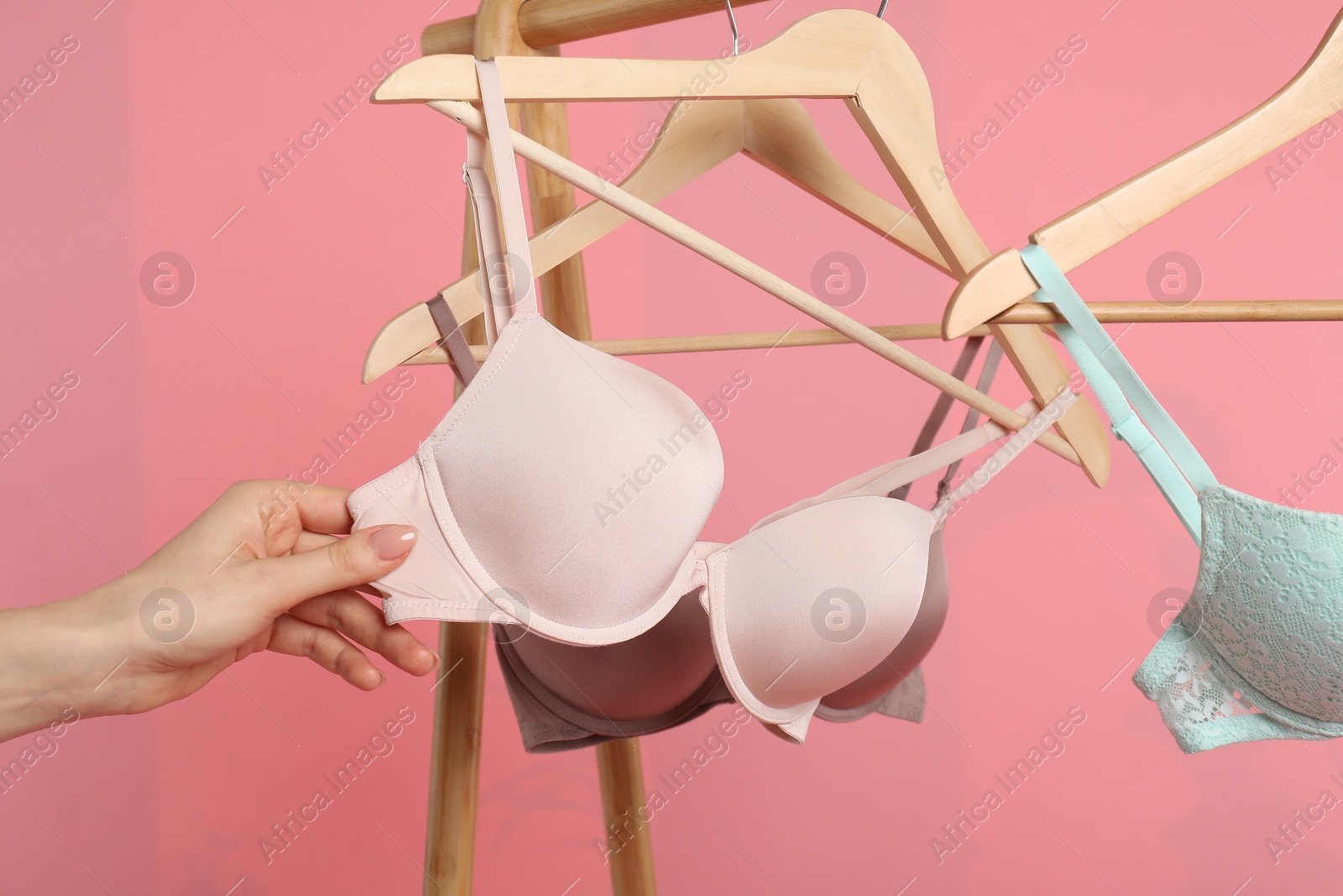 Photo of Woman choosing beautiful bra near rack on pink background, closeup