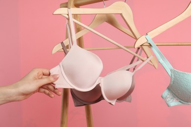 Photo of Woman choosing beautiful bra near rack on pink background, closeup