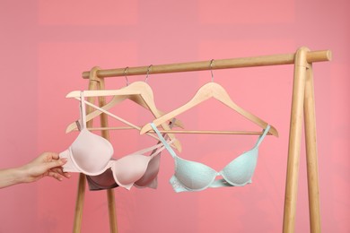 Photo of Woman choosing beautiful bra near rack on pink background, closeup