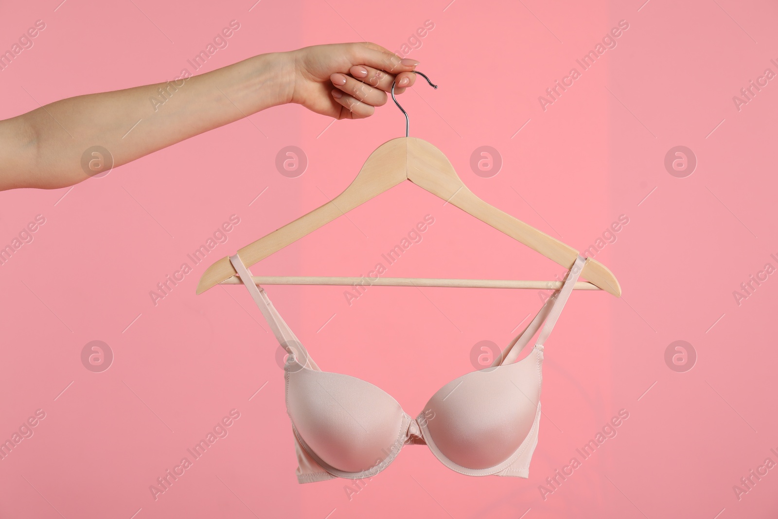 Photo of Woman holding hanger with beige bra on pink background, closeup