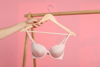 Photo of Woman holding hanger with beige bra on pink background, closeup