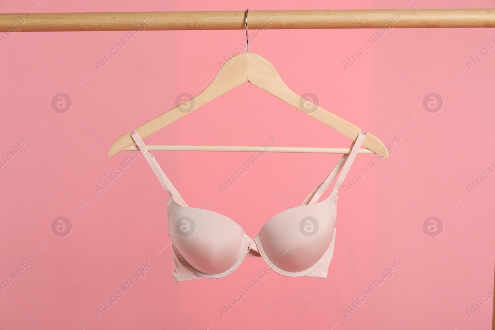 Photo of Hanger with beige bra on wooden rack against pink background