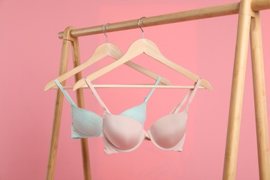 Photo of Hangers with beautiful bras on wooden rack against pink background