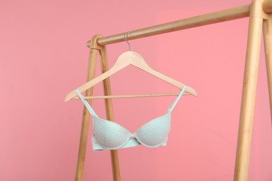 Photo of Hanger with turquoise bra on wooden rack against pink background