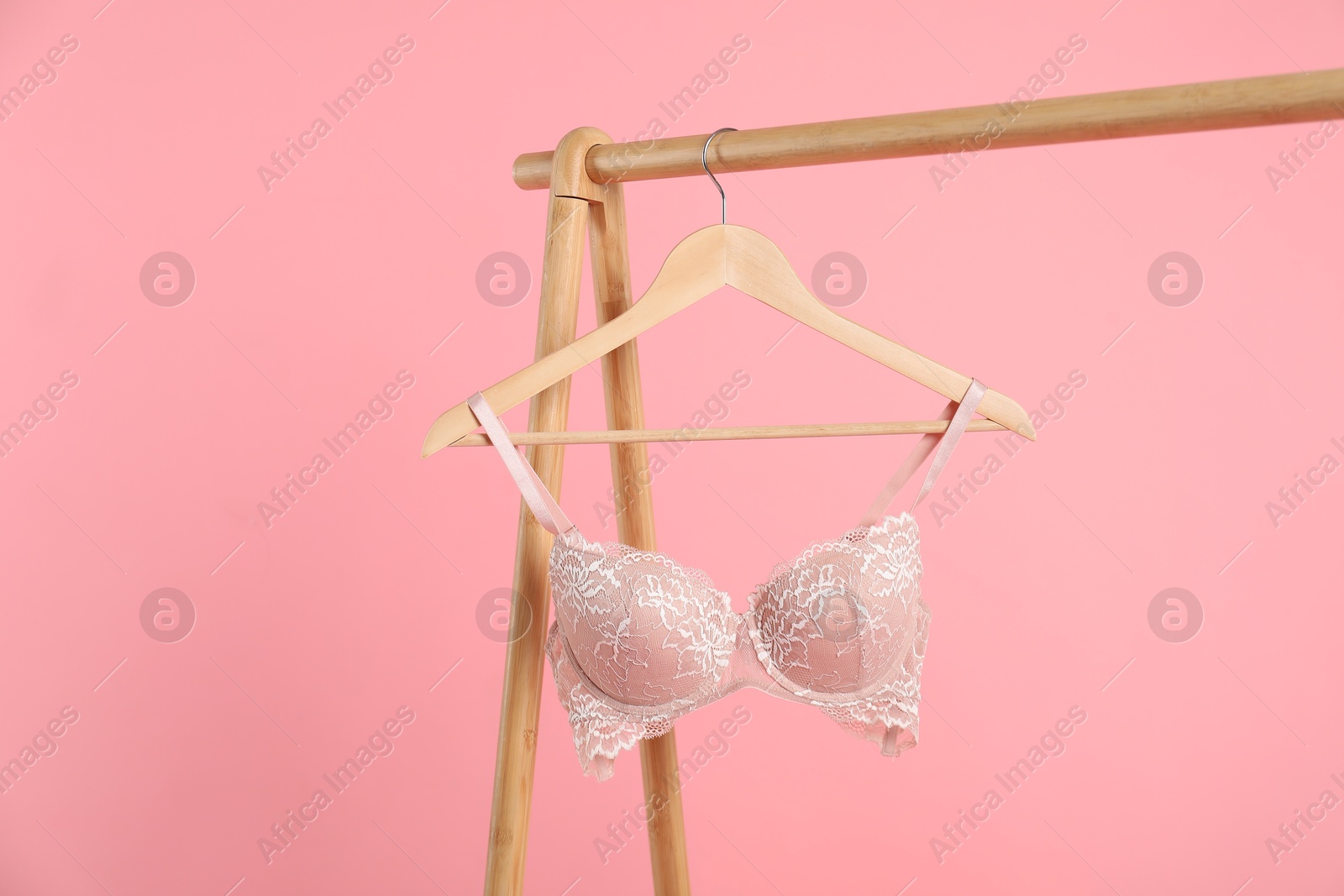 Photo of Hanger with lace bra on wooden rack against pink background, space for text