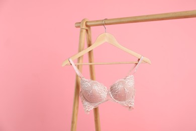 Photo of Hanger with lace bra on wooden rack against pink background, space for text