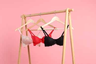 Photo of Hangers with beautiful bras on wooden rack against pink background