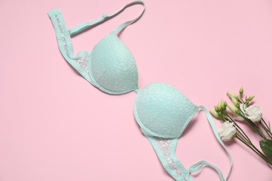 Photo of Beautiful turquoise bra and flowers on pale pink background, flat lay