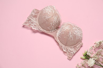 Photo of Beautiful lace bra and flowers on pale pink background, flat lay