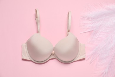 Photo of Beautiful beige bra and feathers on pale pink background, flat lay