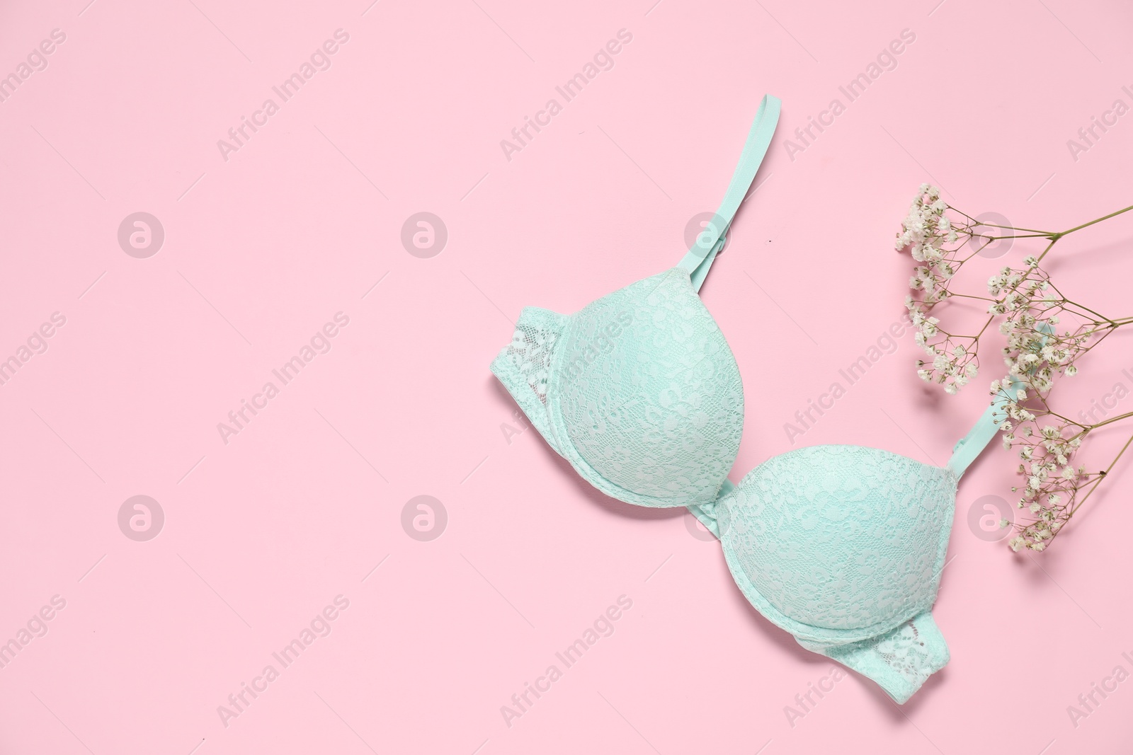 Photo of Beautiful turquoise bra and flowers on pale pink background, flat lay. Space for text