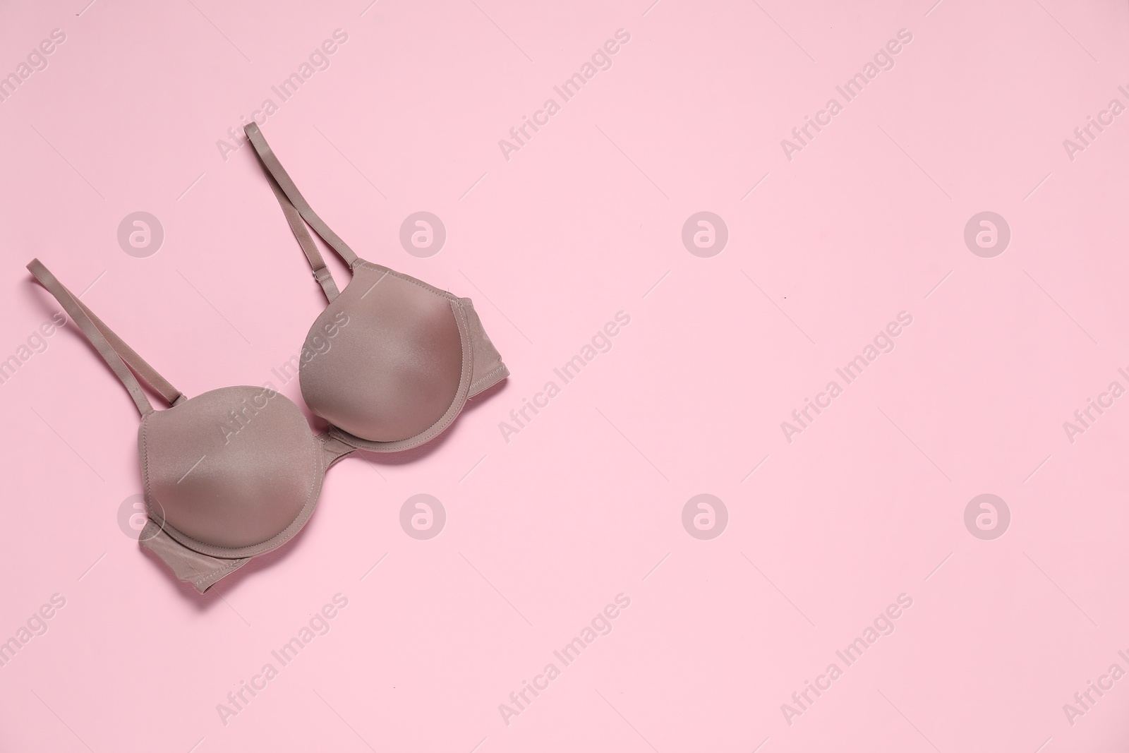 Photo of Beautiful dark beige bra on pale pink background, top view. Space for text