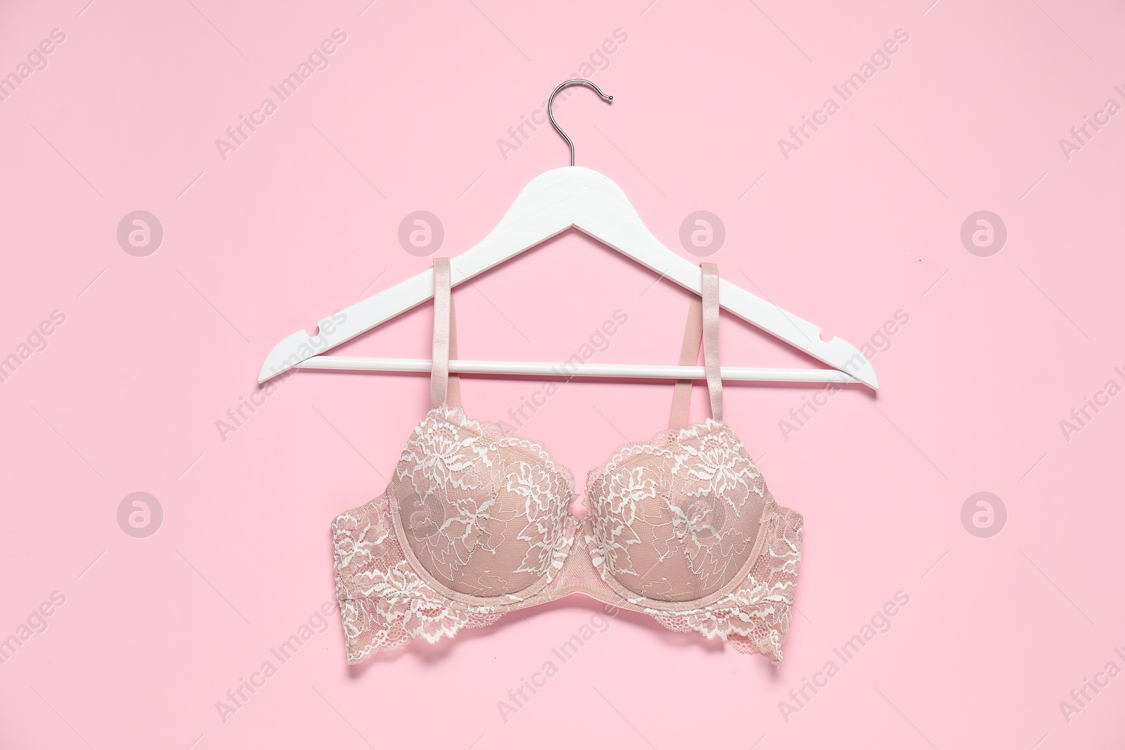 Photo of Hanger with beautiful lace bra on pale pink background, top view