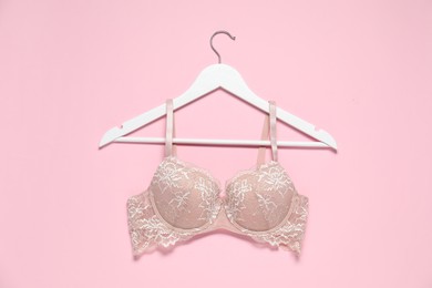 Photo of Hanger with beautiful lace bra on pale pink background, top view