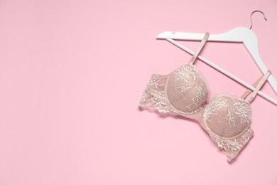 Photo of Hanger with beautiful lace bra on pale pink background, top view. Space for text