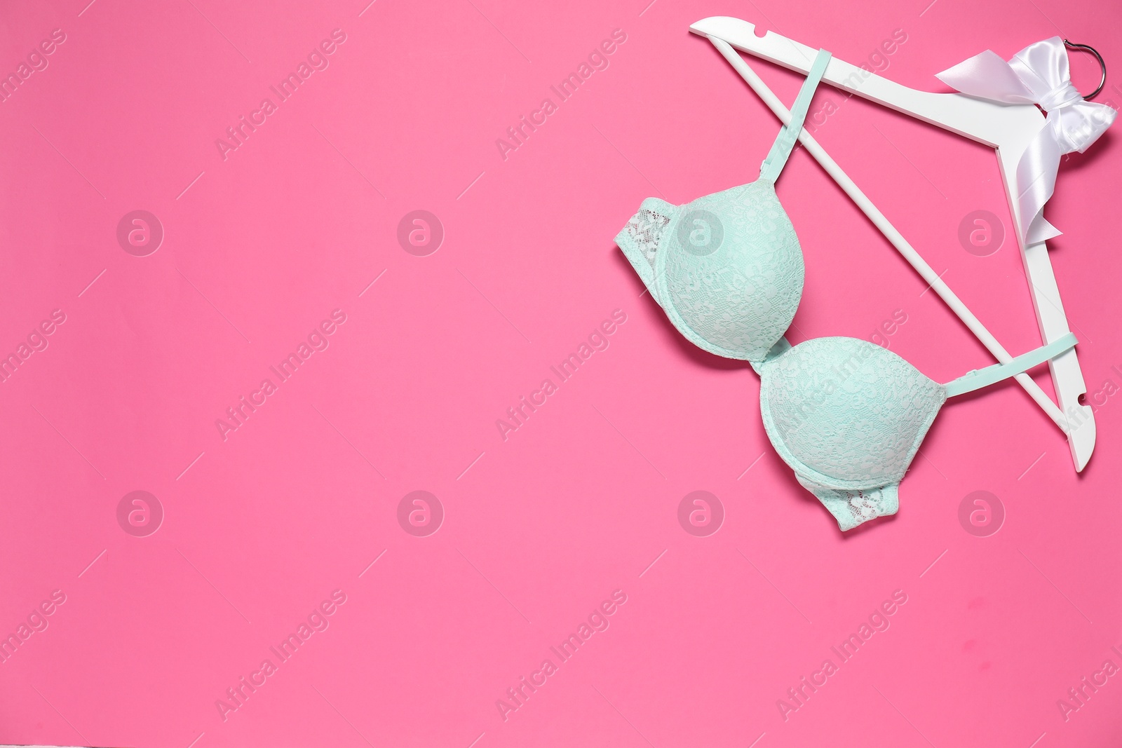 Photo of Hanger with beautiful turquoise bra on pink background, top view. Space for text