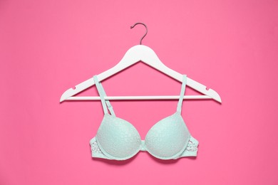 Photo of Hanger with beautiful turquoise bra on pink background, top view