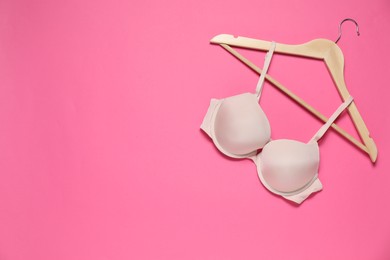 Photo of Hanger with beautiful beige bra on pink background, top view. Space for text