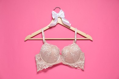 Photo of Hanger with beautiful lace bra on pink background, top view