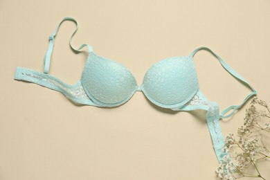 Photo of Beautiful turquoise bra and flowers on beige background, flat lay