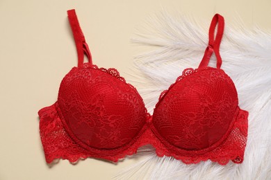 Photo of Beautiful red bra and feathers on beige background, flat lay