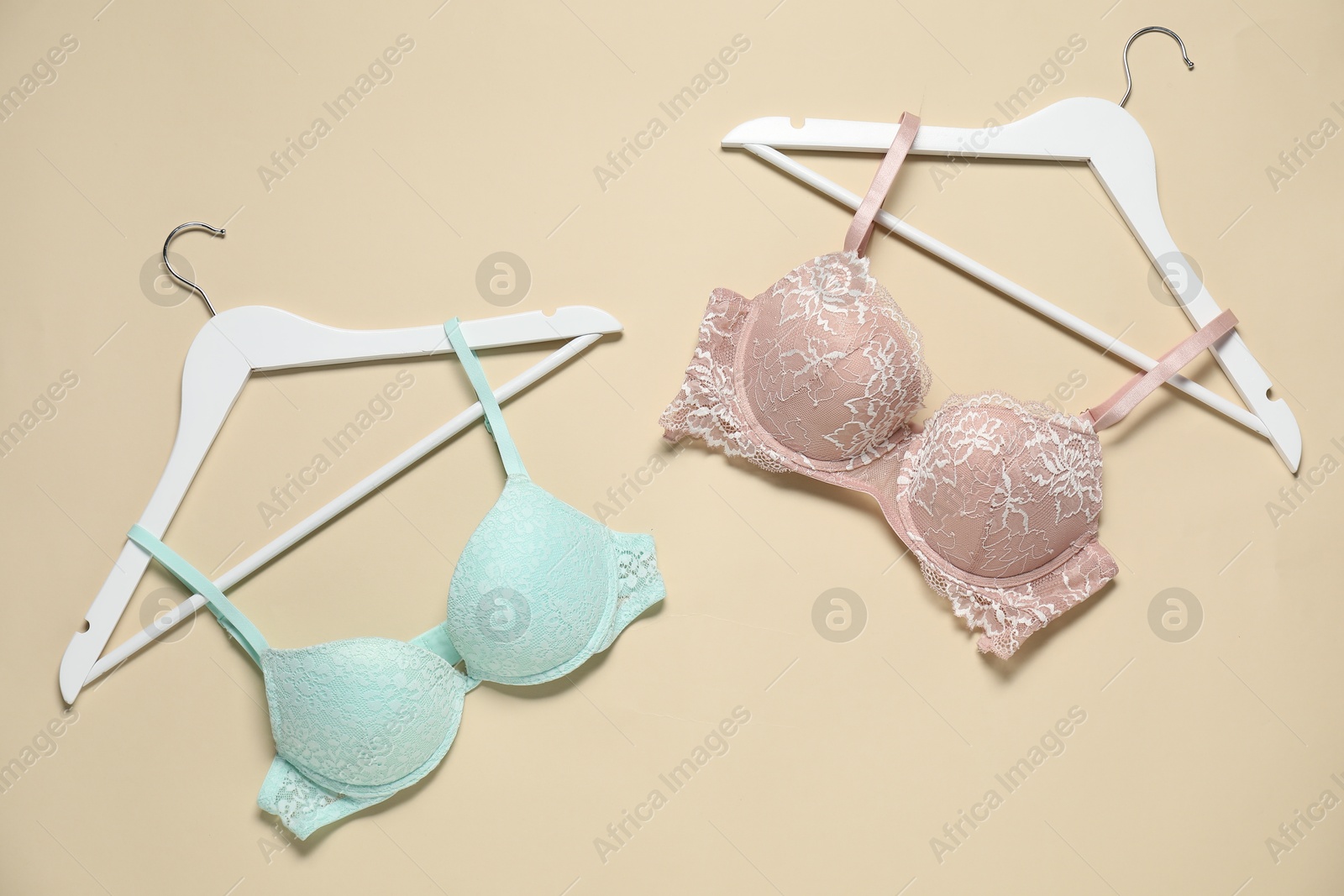 Photo of Hangers with beautiful bras on beige background, flat lay