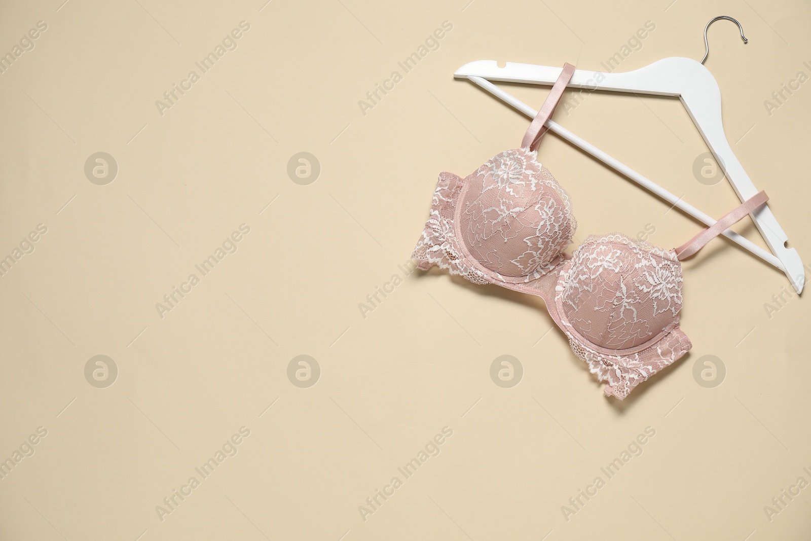 Photo of Hanger with beautiful lace bra on beige background, top view. Space for text