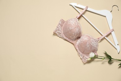 Photo of Hanger with beautiful lace bra and flowers on beige background, flat lay. Space for text