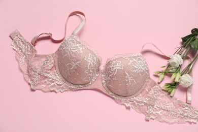 Photo of Beautiful lace bra and flowers on pink background, flat lay