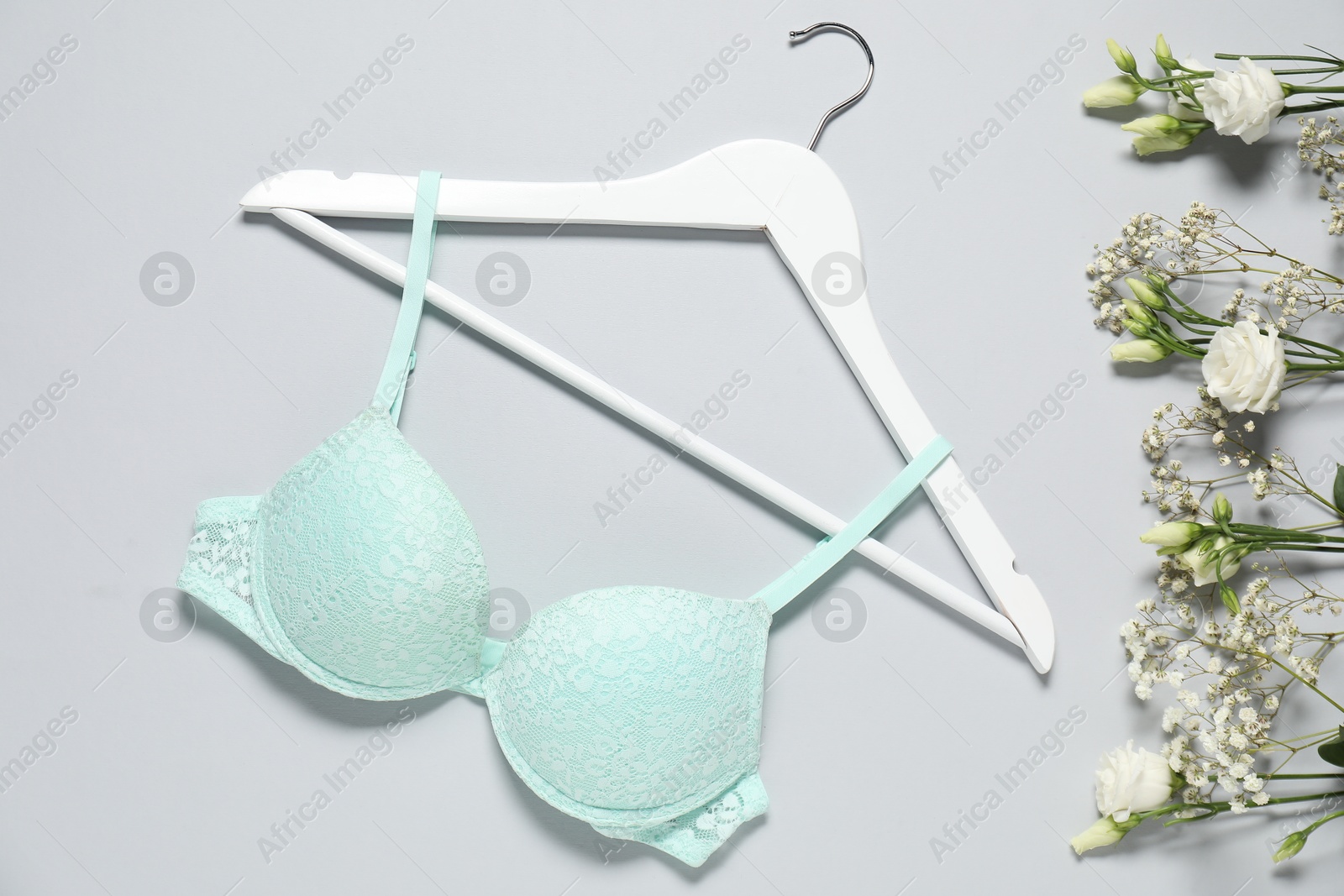 Photo of Hanger with beautiful turquoise bra and flowers on light background, flat lay