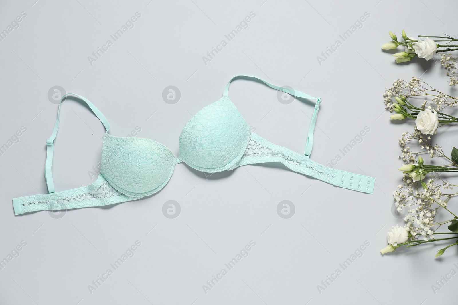 Photo of Beautiful turquoise bra and flowers on light background, flat lay