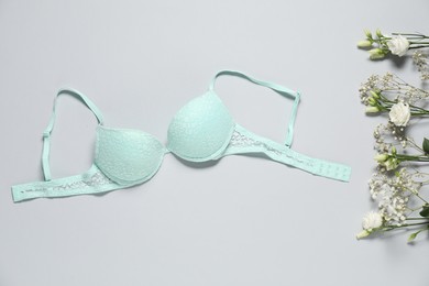 Photo of Beautiful turquoise bra and flowers on light background, flat lay