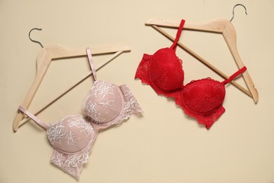 Photo of Hangers with beautiful bras on beige background, flat lay