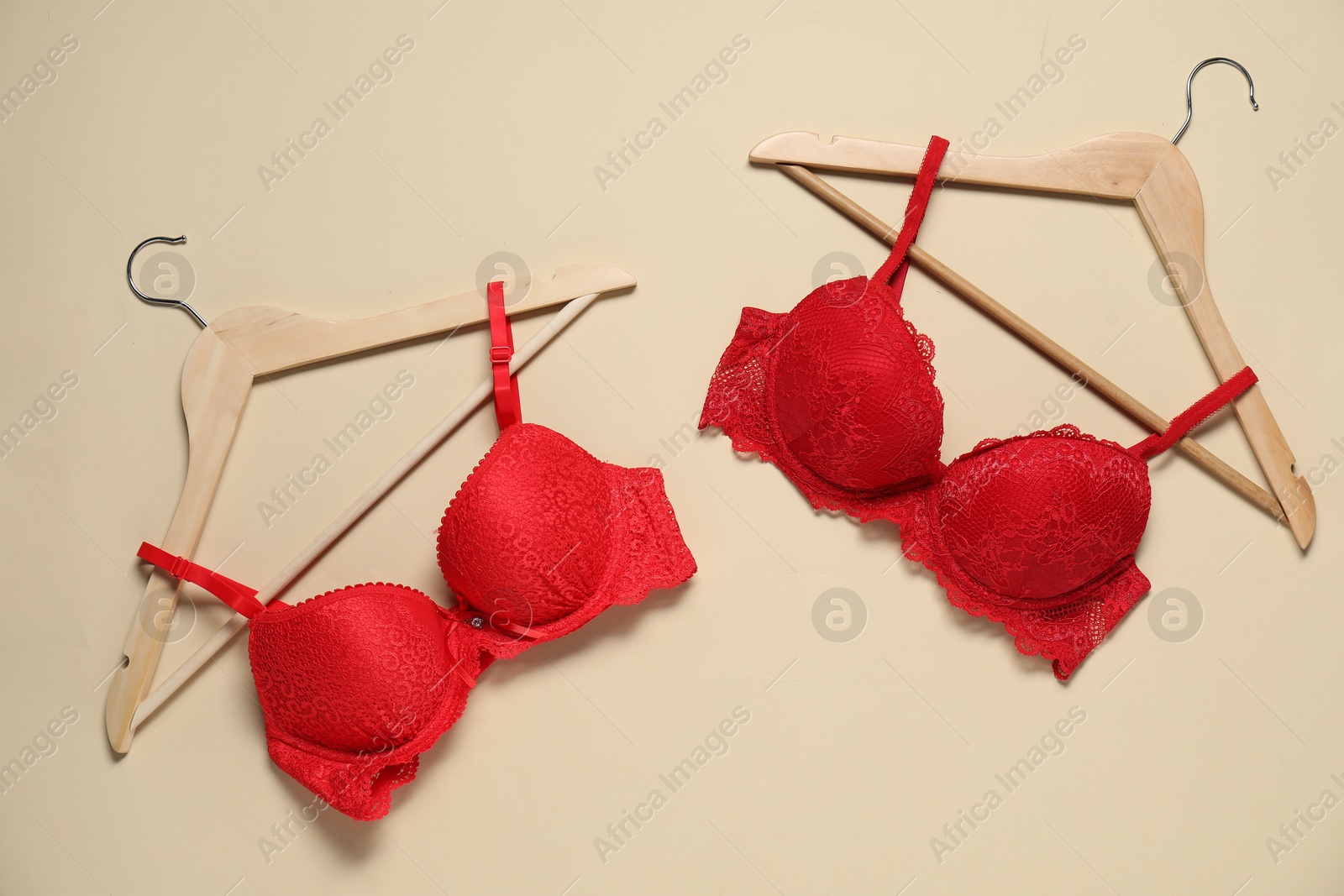 Photo of Hangers with beautiful red bras on beige background, flat lay