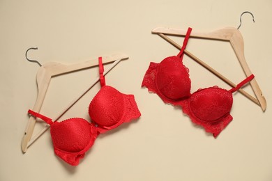 Photo of Hangers with beautiful red bras on beige background, flat lay