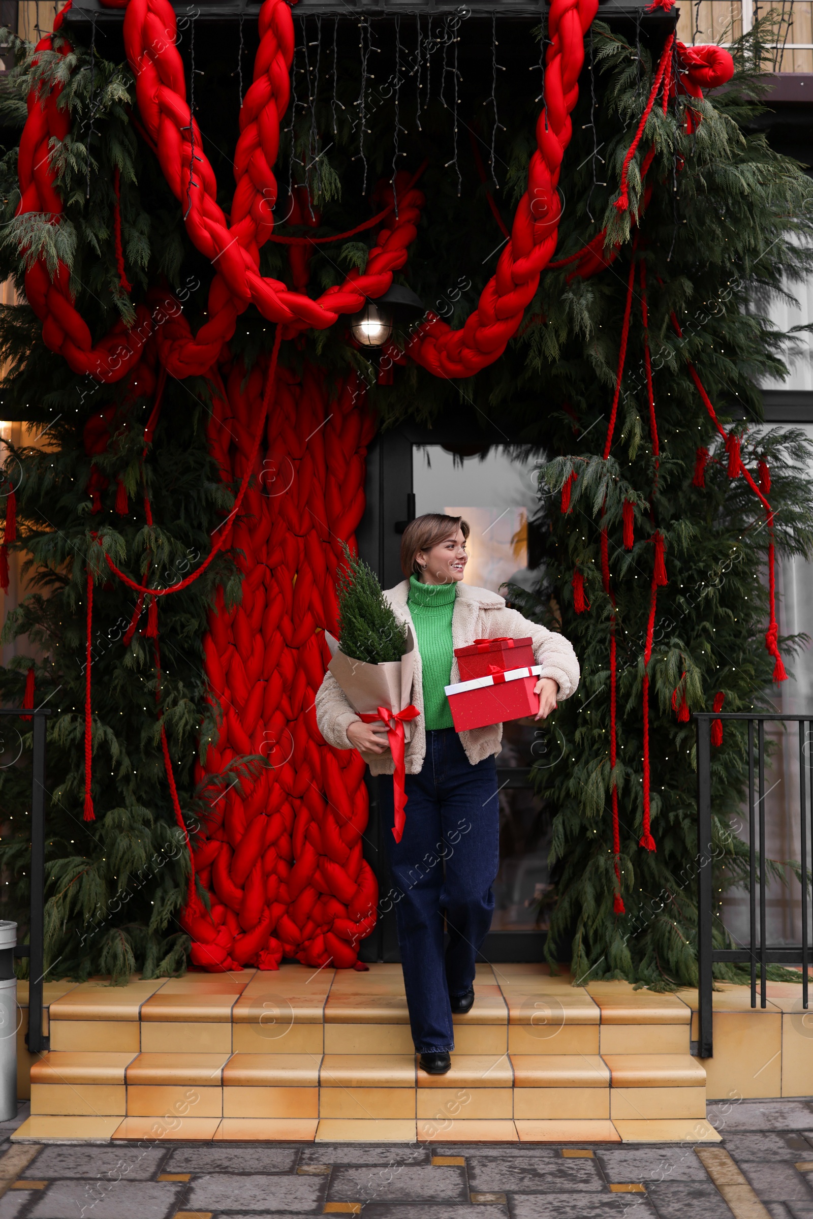 Photo of Happy woman with thuja tree and Christmas gifts going out from shop outdoors