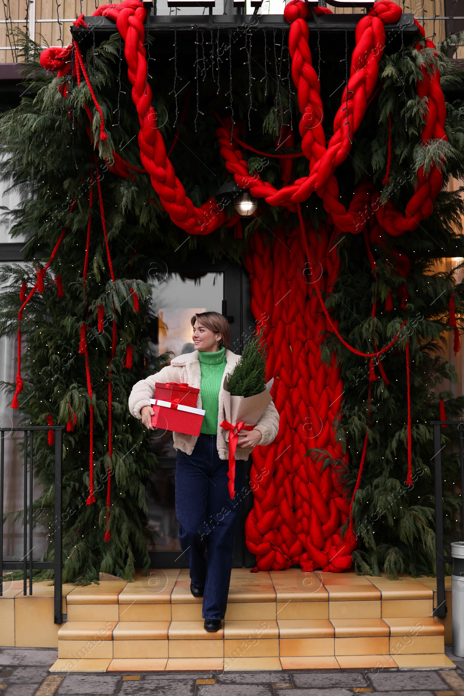 Photo of Happy woman with thuja tree and Christmas gifts going out from shop outdoors