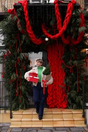 Photo of Happy woman with thuja tree and Christmas gifts going out from shop outdoors