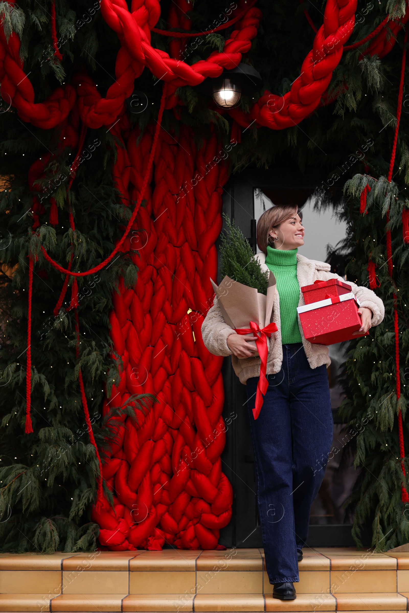 Photo of Happy woman with thuja tree and Christmas gifts going out from shop outdoors