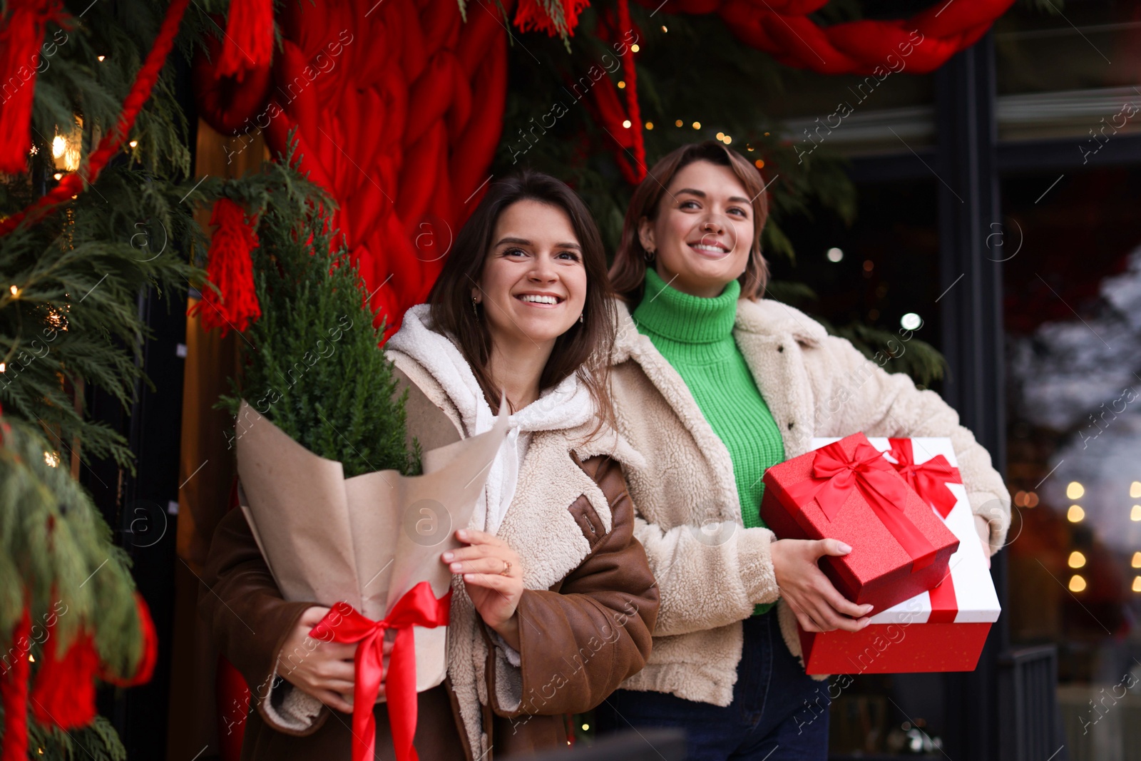 Photo of Happy friends with thuja tree and Christmas gifts near shop outdoors