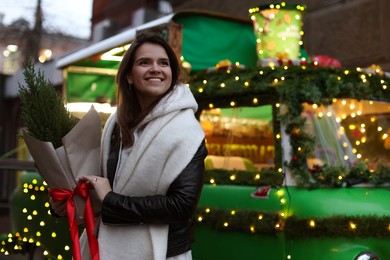 Photo of Happy woman with thuja tree near Christmas bus outdoors. Space for text