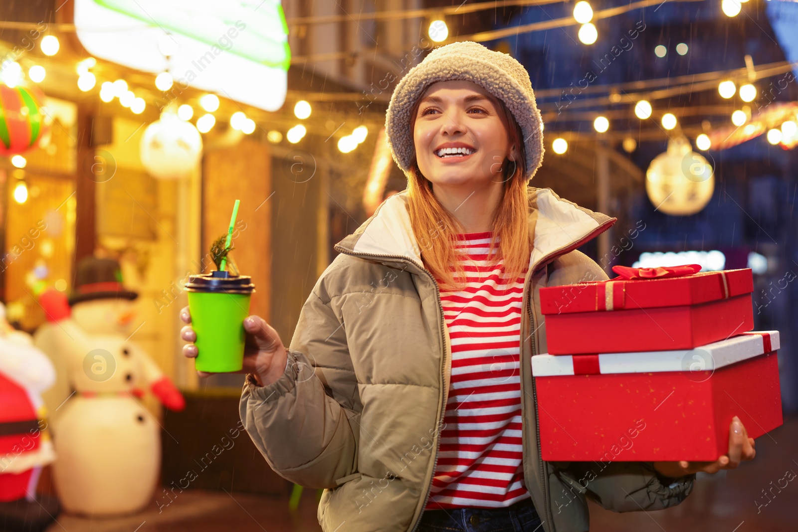 Photo of Happy woman with Christmas gifts and paper cup at fair