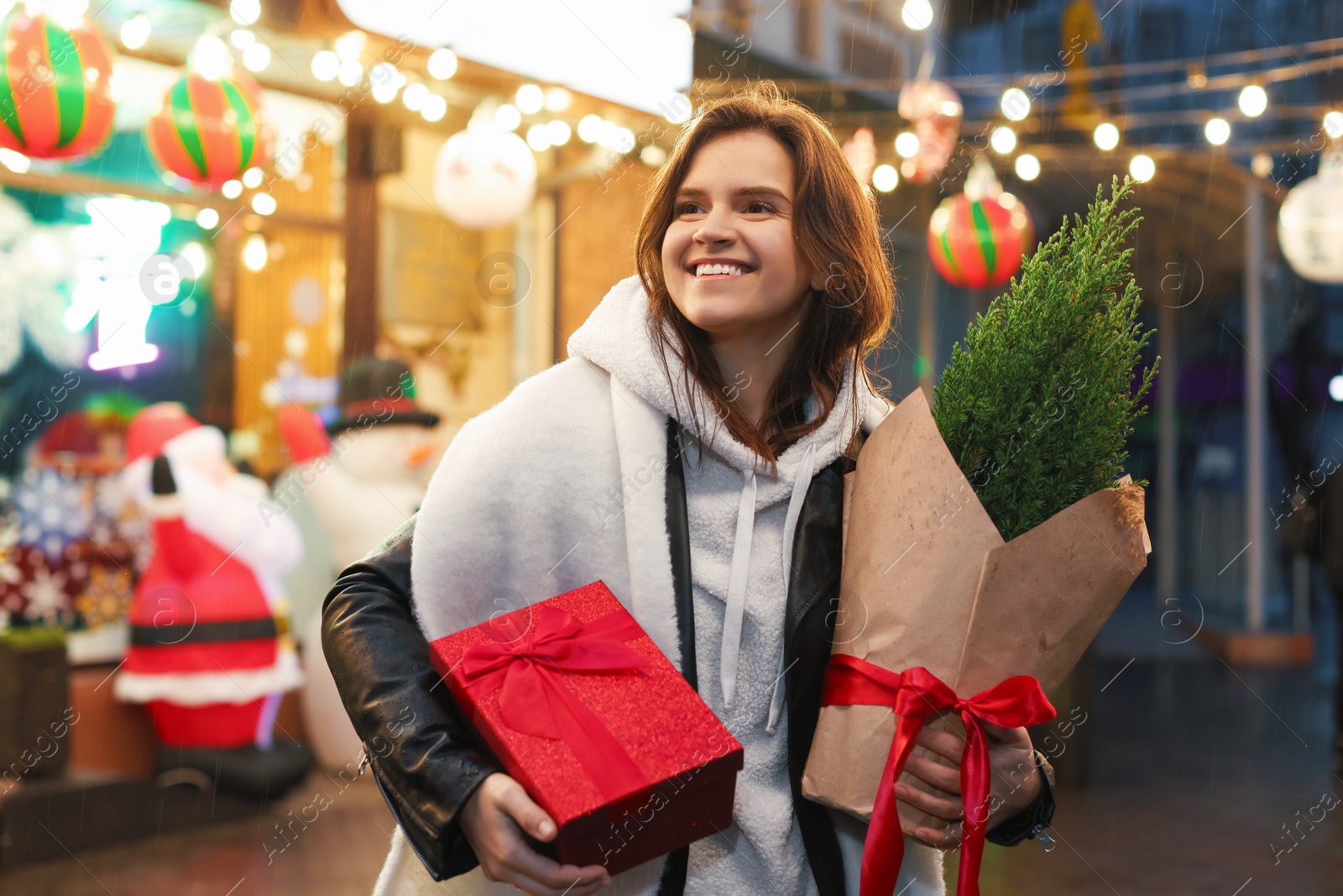 Photo of Happy woman with Christmas gift and thuja tree at fair